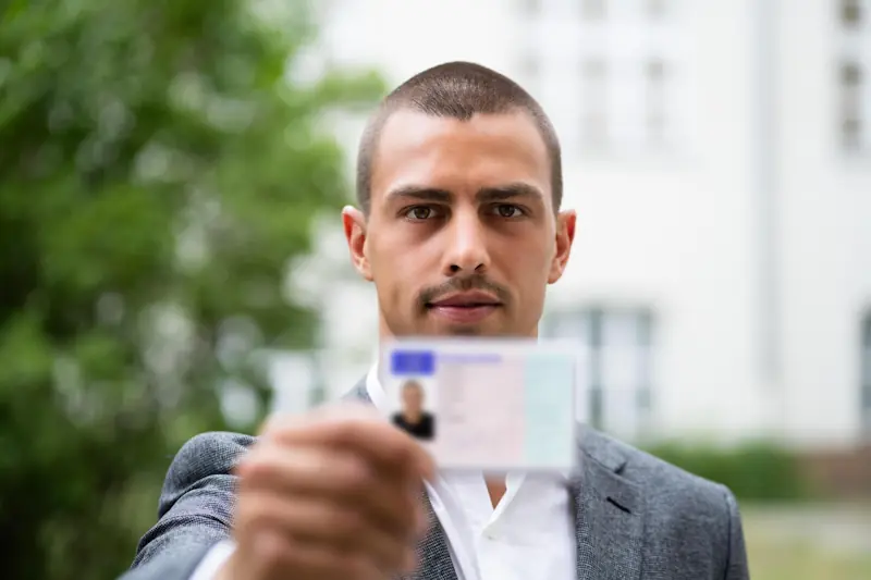 Mann in Anzug hält eine Ausweiskarte in die Kamera